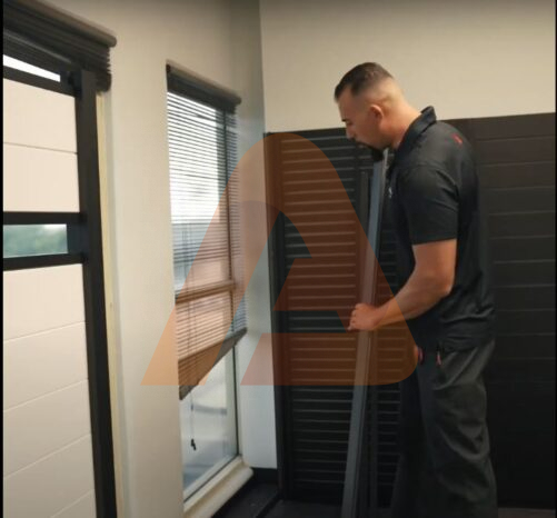 Contractor aligning a three-way aluminum fence post during DIY fence installation indoors.