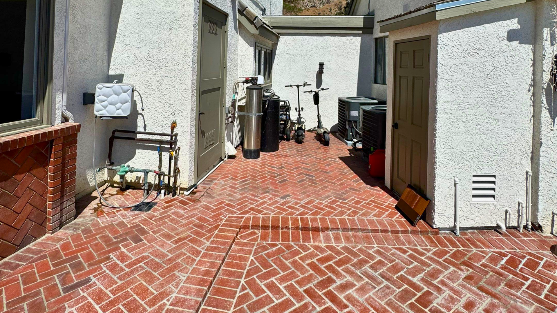 Residential backyard with red brick herringbone patio and exterior utility area