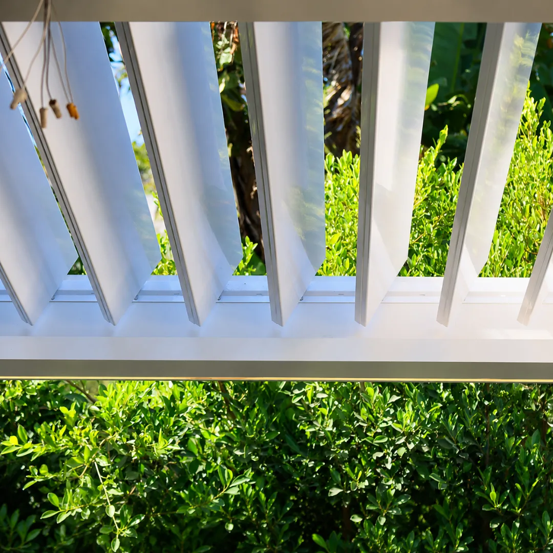 Close-up of white automatic louver blades partially open for filtered sunlight