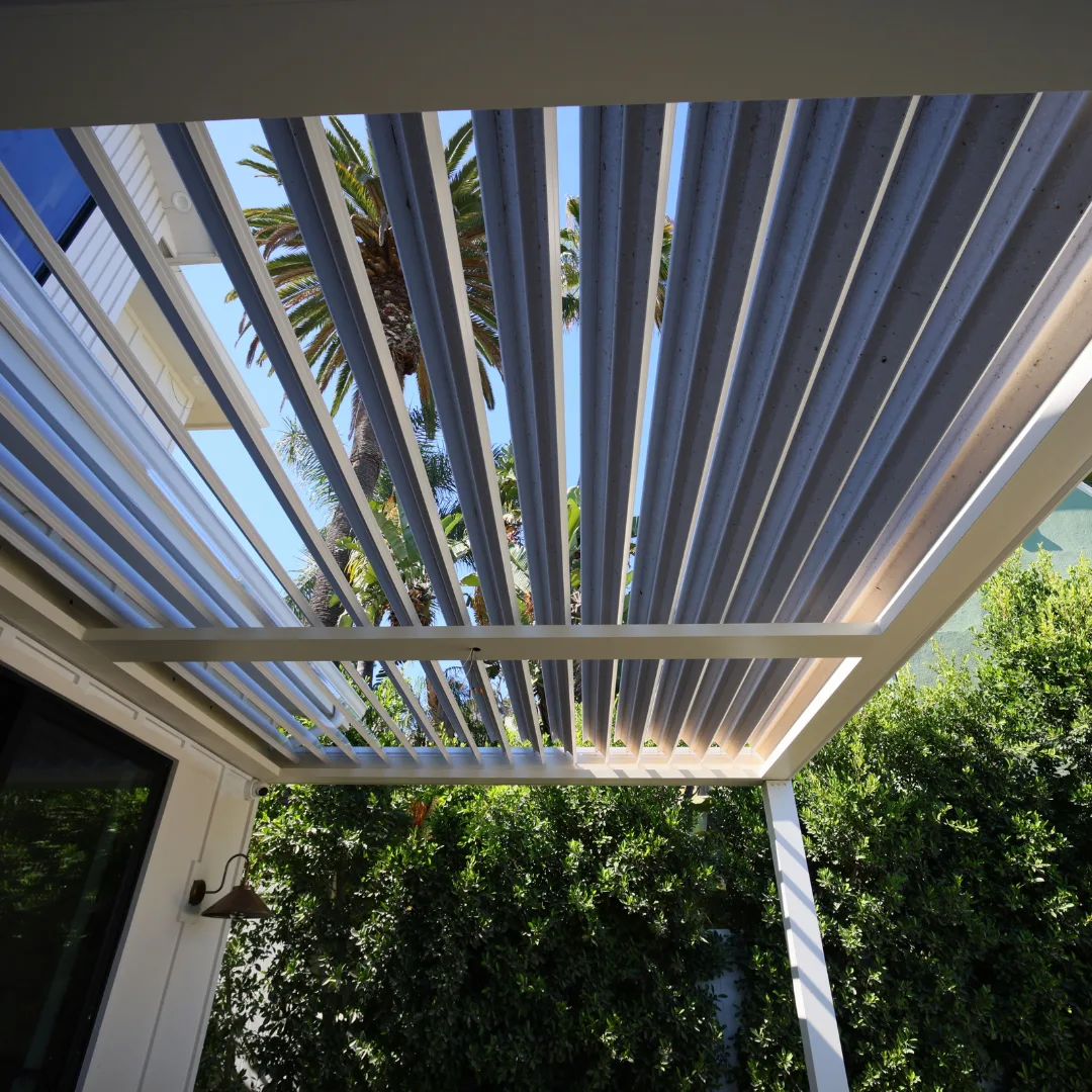 White adjustable aluminum louver blades partially open above a patio