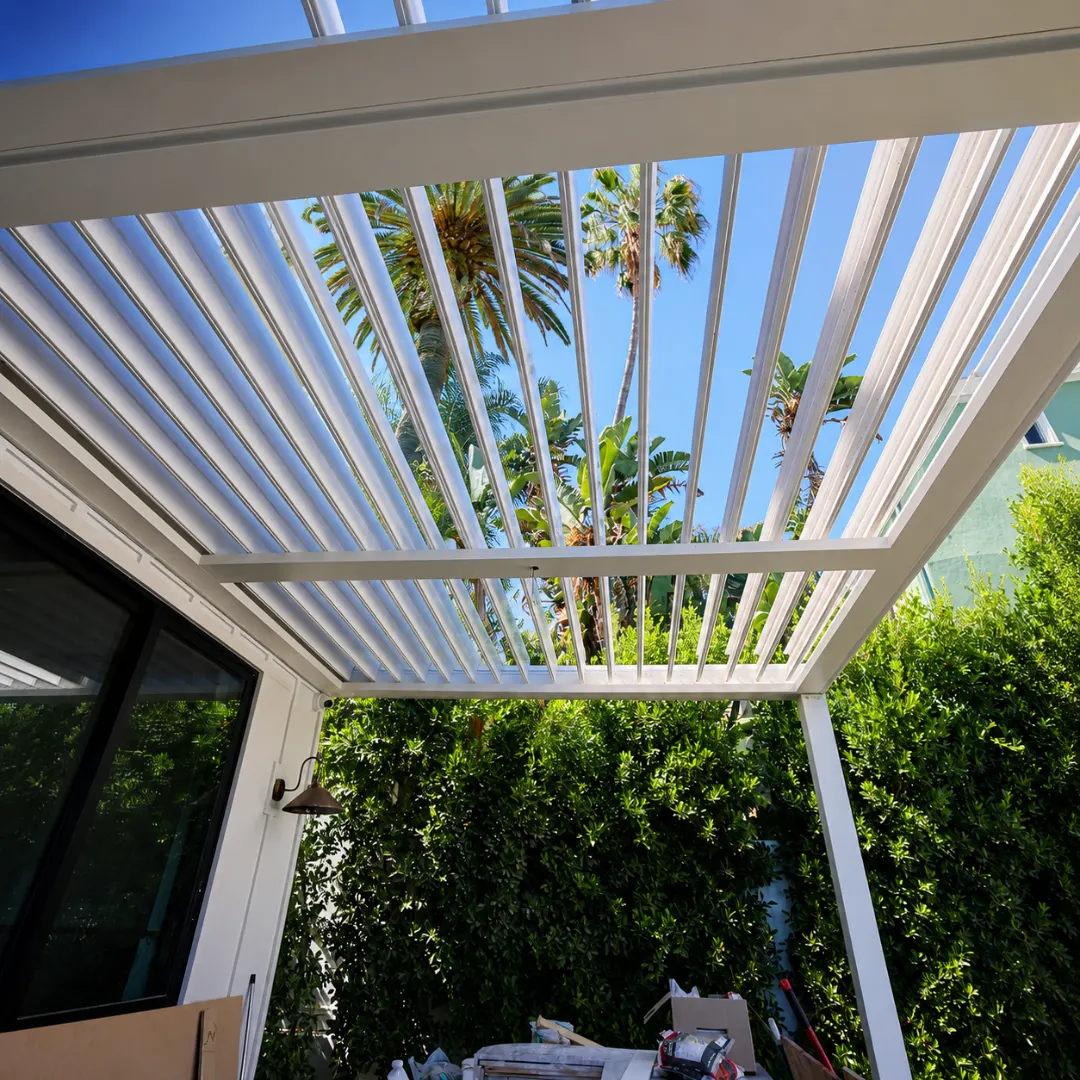 White automatic louver patio roof open beneath palm trees
