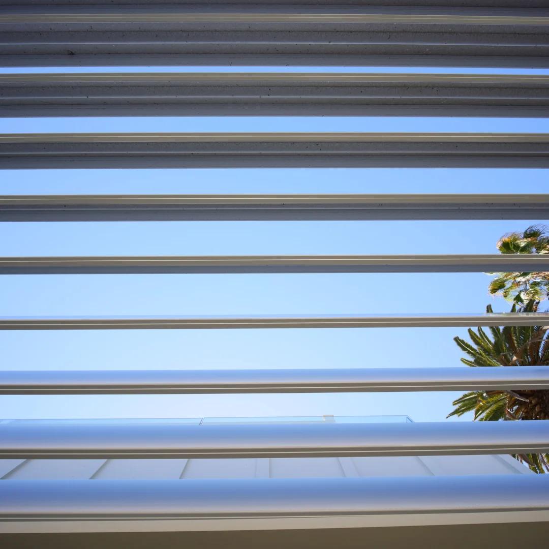 Close-up of open white aluminum louver blades against a blue sky