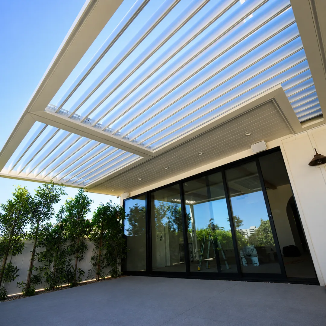 White automatic louver patio roof open above black sliding glass doors