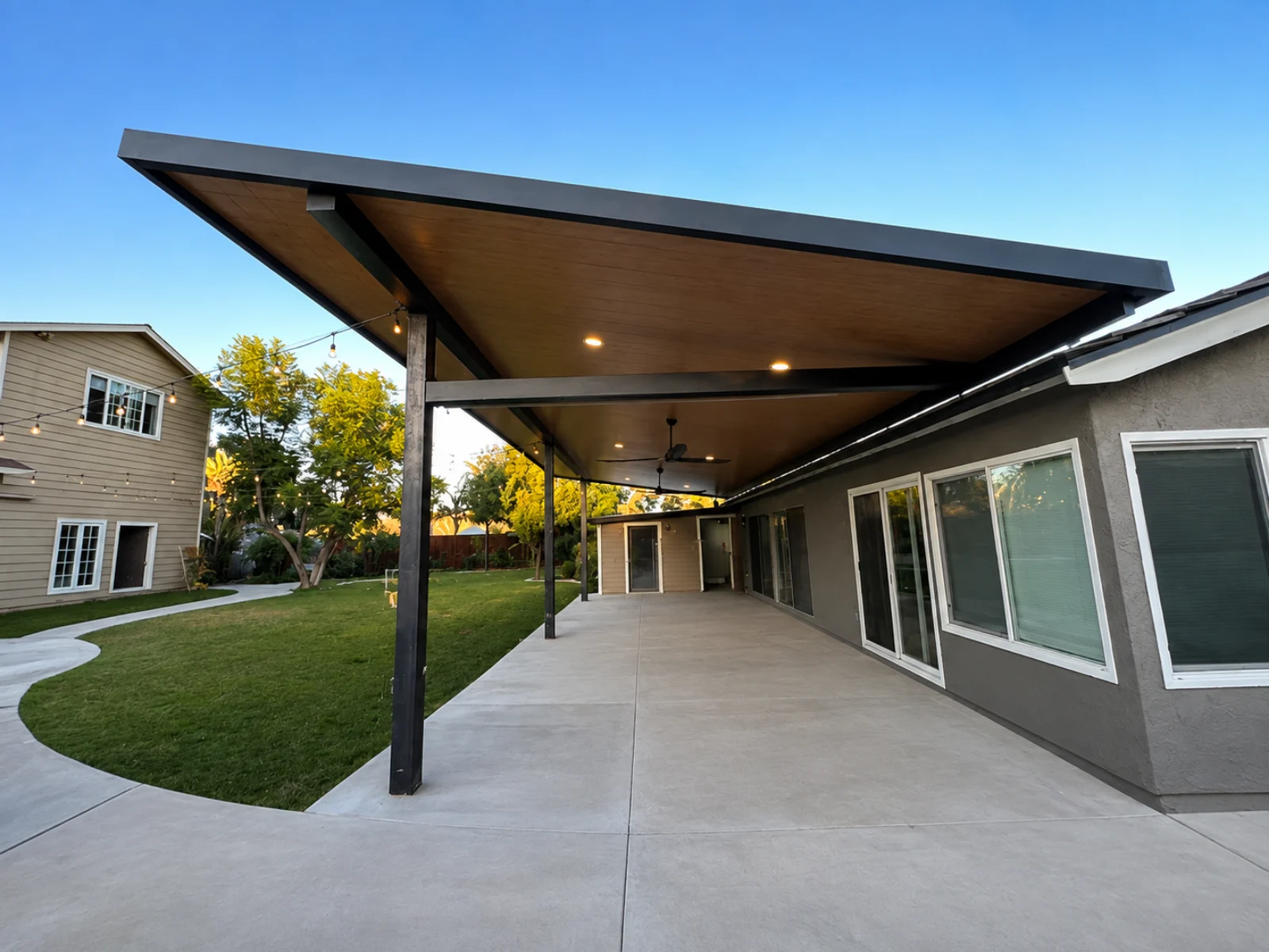 Large attached insulated aluminum patio cover with a wood-look ceiling, recessed lights, and a fan over a backyard patio
