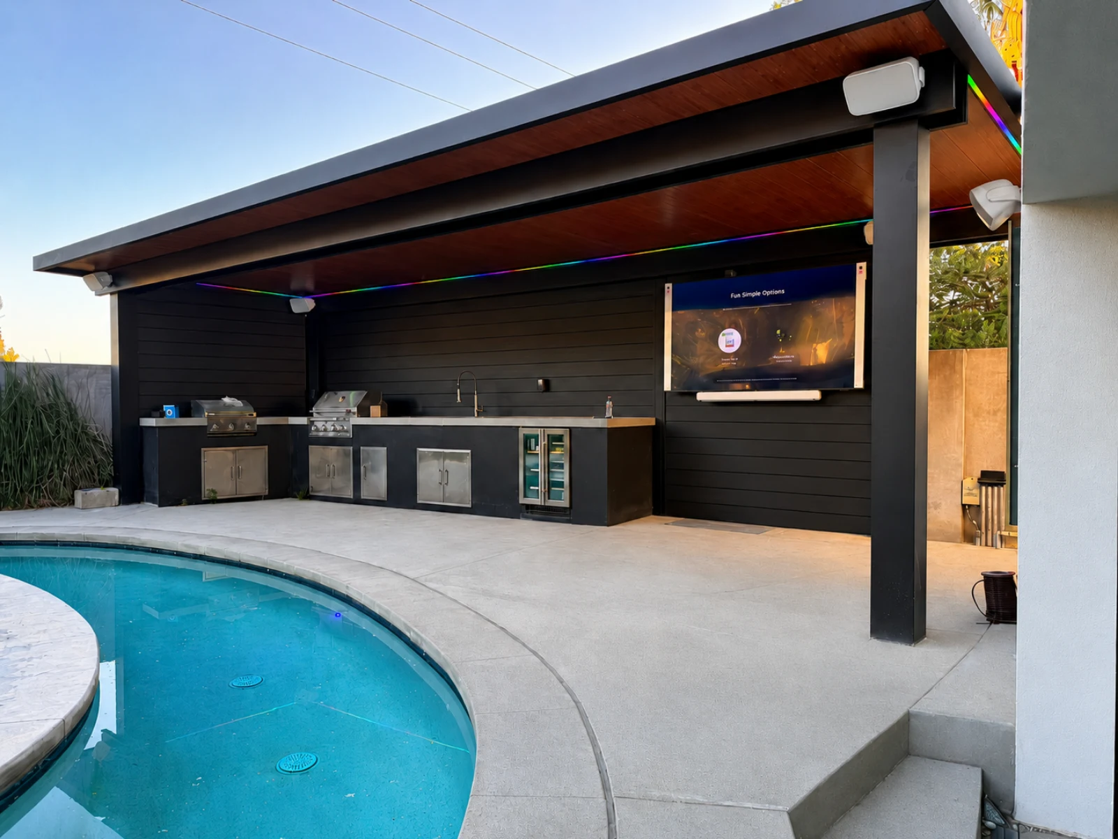 Insulated aluminum patio cover with a wood-look ceiling over an outdoor kitchen beside a swimming pool