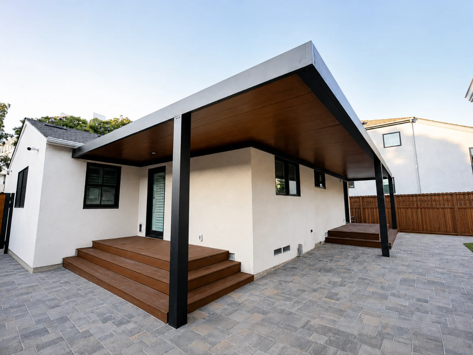 Insulated aluminum patio cover wrapping a white home with a wood-look ceiling and black support posts