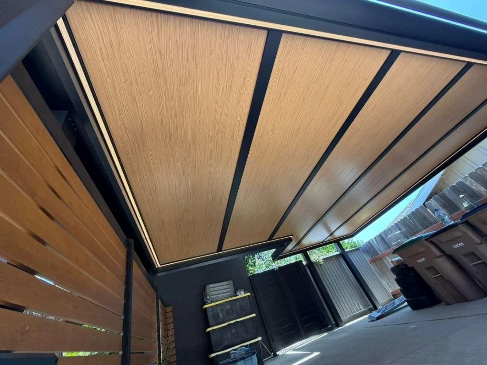 Close-up underside of wood-look insulated aluminum roof panels within a black patio cover frame