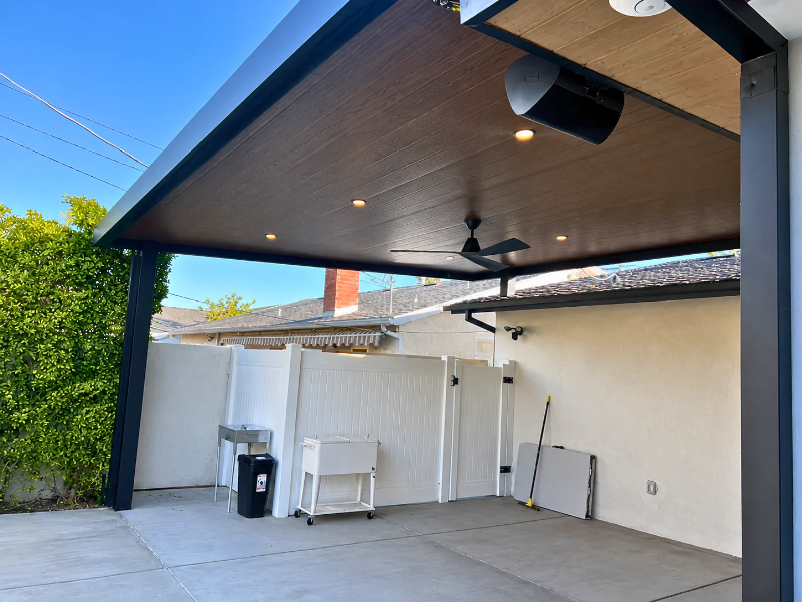 Wood-look insulated aluminum patio cover with a ceiling fan and recessed lights over a residential driveway