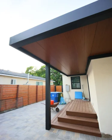 L-shaped insulated aluminum patio roof system sheltering residential back entrance and raised deck stairs.