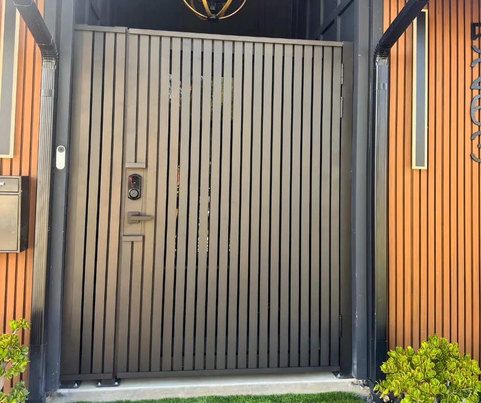 Black vertical-slat entry gate beside architectural wood-look cladding