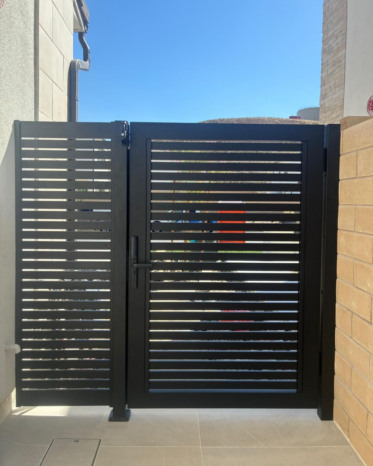 Custom black aluminum pedestrian swing gate with heavy-duty hinges mounted to brick wall.