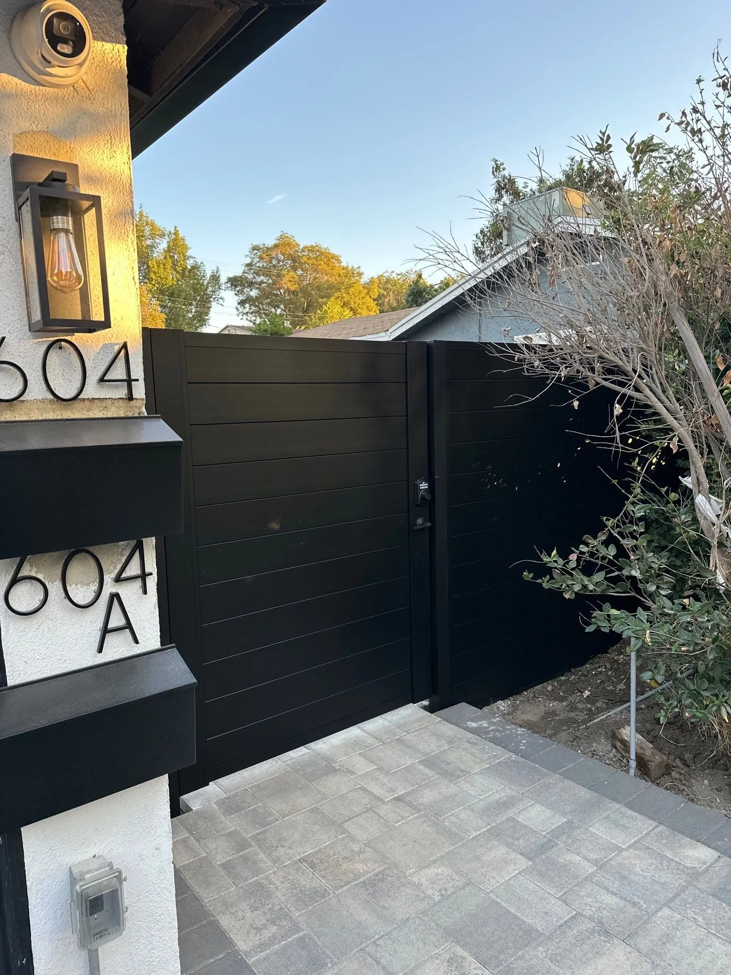 Black-finished horizontal-slat gate and adjoining panels at a residential entrance