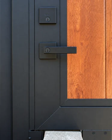 Detail of textured matte black electronic handle lock contrasting against warm timber woodgrain aluminum panel.