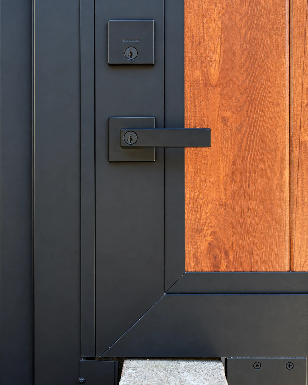 Detail of textured matte black electronic handle lock contrasting against warm timber woodgrain aluminum panel.