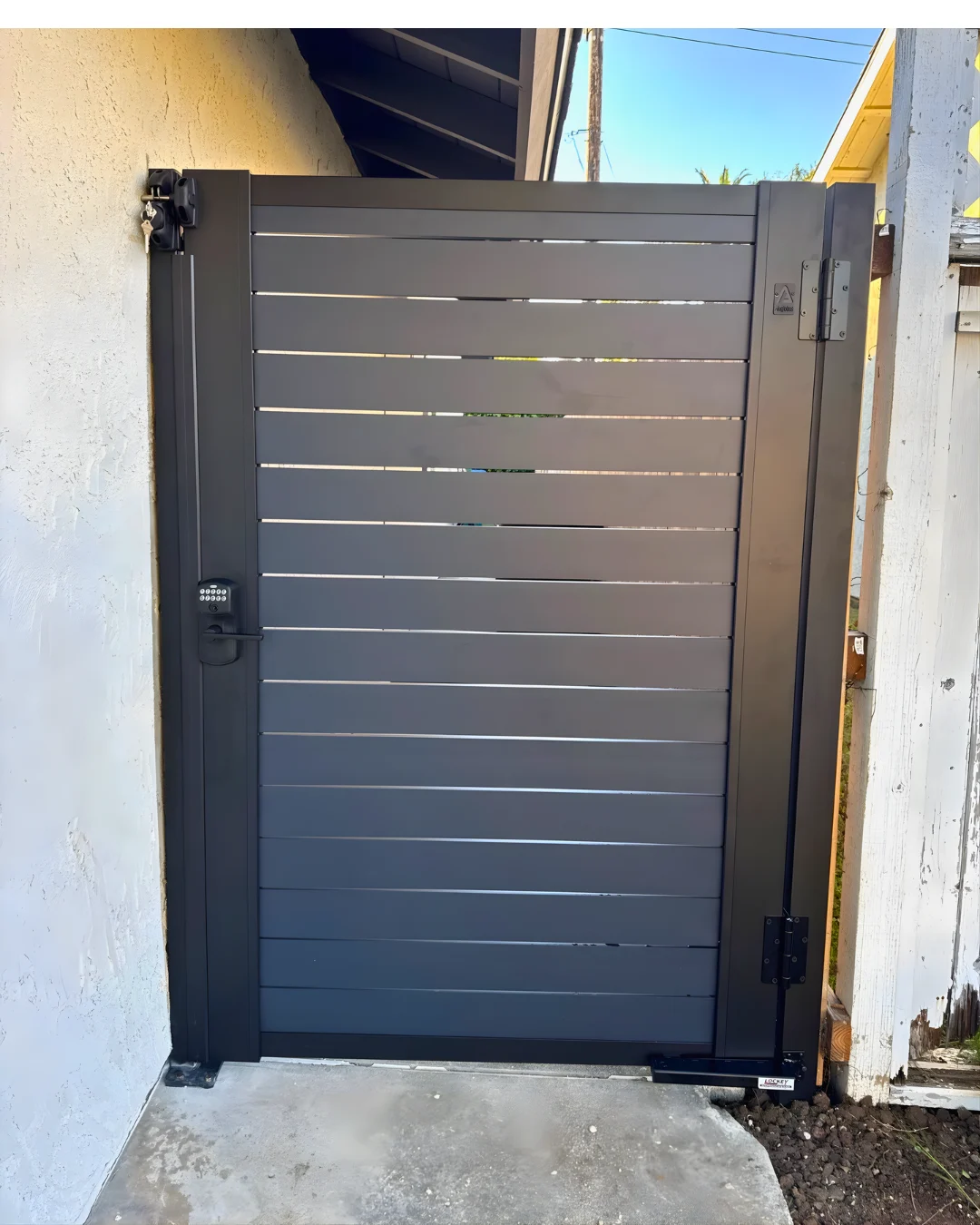 Black aluminum pedestrian gate with horizontal slats in a side passage