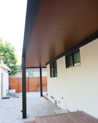 L-shaped insulated aluminum patio roof system sheltering residential back entrance and raised deck stairs.
