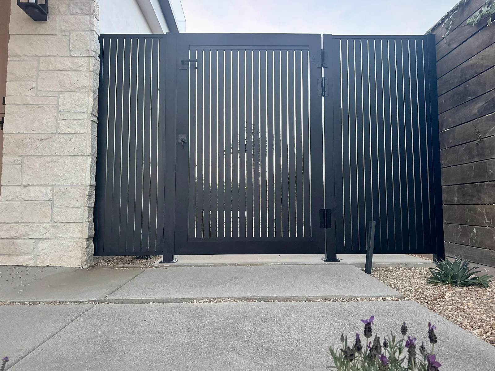 ALU20 vertical slat black gate beside a stone facade