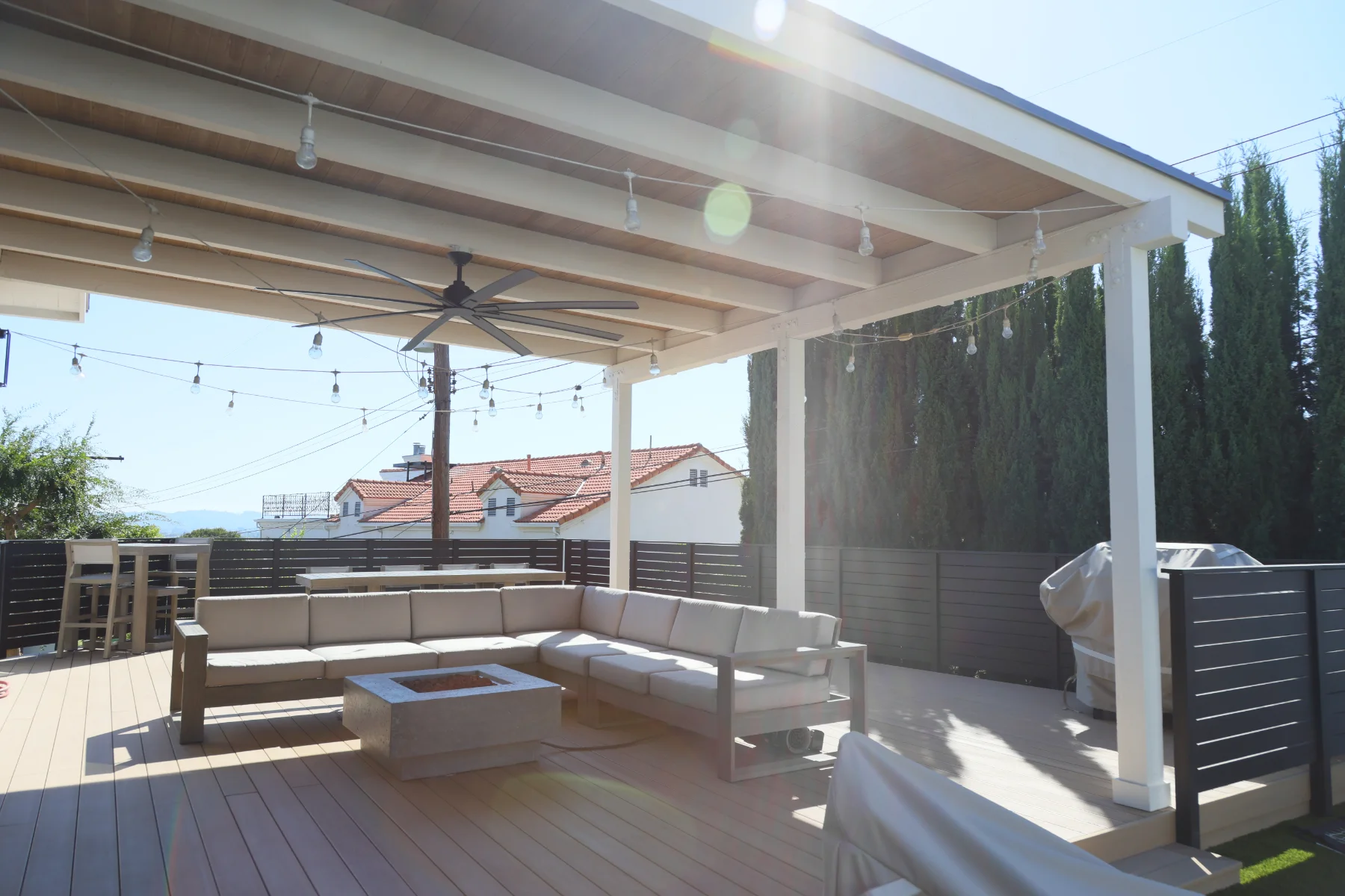 White patio cover with ceiling fan and string lights over a lounge deck